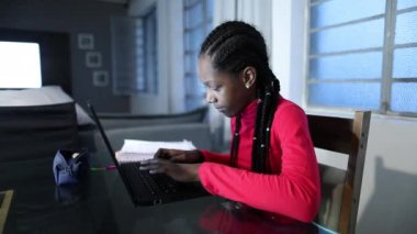 Teen black girl typing on computer laptop at home