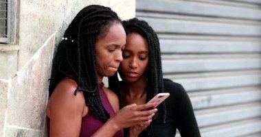 Afrikalı anne ve kız cep telefonu ekranına bakıyor.