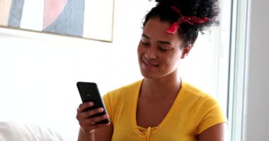 Gülümseyen cep telefonu aygıtı kullanan gizli bir zenci kız. Genç bir kadın evde oturuyor ve telefonda yazıyor.