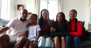 Siyahi Afrikalı aile, evdeki koltukta fotoğraf çektirmek için birlikte poz veriyor.