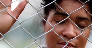 Metal parmaklıklardan bakan üzgün Afrikalı Amerikalı kadın. Güney Amerikalı çitlere tutunuyor