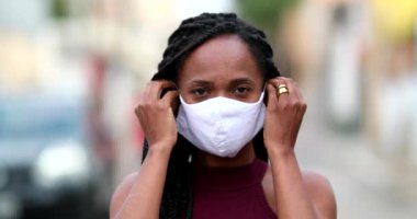 Woman putting covid-19 face mask prevention in urban street, black African ethnicity