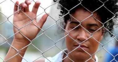 Metal çit tutan dalgın, üzgün siyah kadın