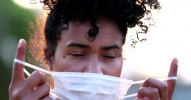 Mutlu melez genç kadın covid-19 yüz maskesi çıkarıyor, salgının sonu, rahatlama hissi