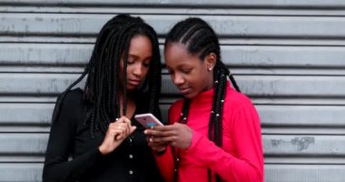 African teen girls using cellphone together, Black teen girlfriends smiling and laughing holding smartphone