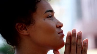 Hopeful Black african woman praying outside, feeling happy and faithful