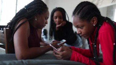 Family in front of smartphones. Black African daughter and mother looking at cellphone at home