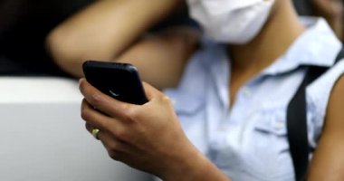 Commuter african woman wearing face mask checking cellphone while riding subway