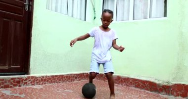 Afrikalı çocuk topla oynuyor, siyah çocuk tek başına spor yapıyor.