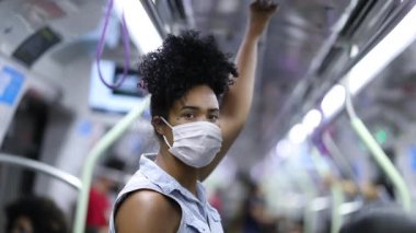Young African woman standing at metro looking at camera with surgical mask virus prevention