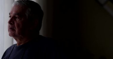 Thoughtful senior standing by window in meditation, good for transition