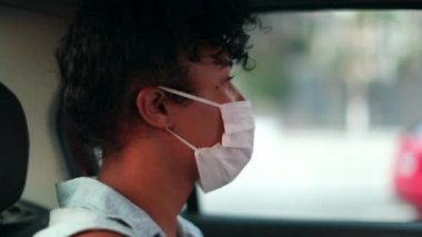 Passenger girl in taxi backseat wearing pandemic mask looking out car window