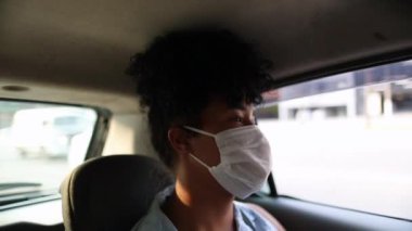 Passenger wearing surgical mask riding taxi during pandemic, black african american woman looking out car window