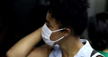 Yüzü maskeli Afrikalı bir kadın metroya binerken cep telefonunu kontrol ediyor.