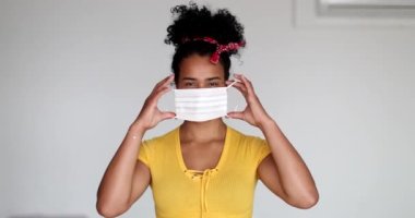 Young African descent woman putting face mask virus prevention, girl crossing arms looking at camera