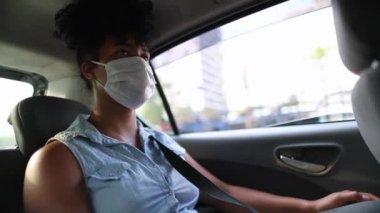 Black girl wearing surgical mask in backseat taxi looking at cellphone screen
