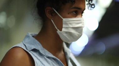 Young black woman checking cellphone waiting for metro train to arrive. African american commuter wearing virus prevention mask