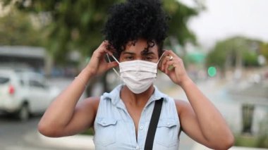 Young african american woman putting mask virus prevention in urban city in background