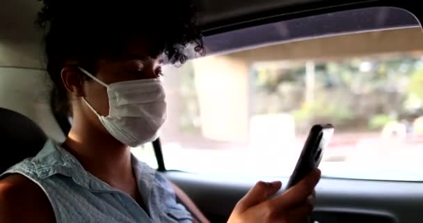 後部座席の乗客の女の子流行のウイルスマスクを身に着けているタクシースマートフォンを見て — ストック動画
