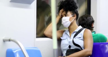 Afro-Amerikalı kadın metroda salgın sırasında cep telefonunu kontrol ediyor.