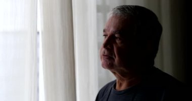 Depresyonda olan yaşlı adam, pencerenin kenarında gölgede duruyor.