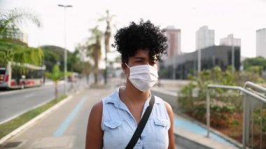 Young woman walking in city with surgical mask prevention against pandemic. African descent girl walking