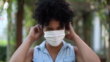 Young black woman putting covid mask outside. African american girl puts surgical mask walking forward