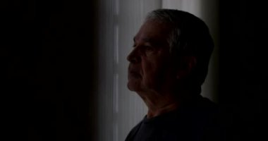 Düşünceli kıdemli adam pencerenin yanında dışarı bakıyor.