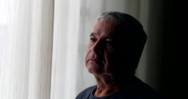 Thoughtful older man standing by window thinking. Pensive senior person