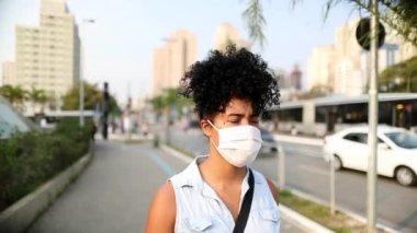 Young african american woman walking in city wearing surgical mask in downtown city