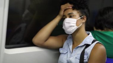 Pensive black woman commuter in underground subway metro wearing surgical mask