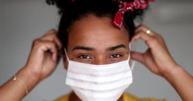 Young African descent woman putting face mask virus prevention, girl looking at camera
