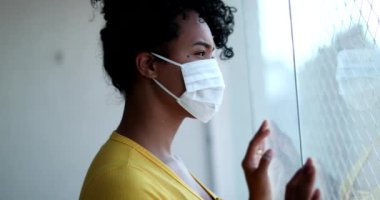 Pencere kenarında duran Afrikalı kadın virüse karşı salgın maskesi takıyor.