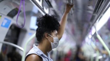 Black girl standing at subway train wearing virus surgical mask
