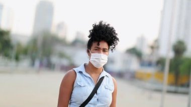 Young mixed race woman standing wearing virus mask. Portrait black girl looking at camera during pandemic