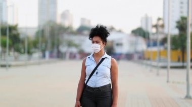 Young african american woman standing outside wearing pandemic virus mask