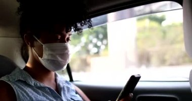 Taksi arka koltuğunda salgın maskesi takan ve cep telefonu ekranına bakan yolcu.