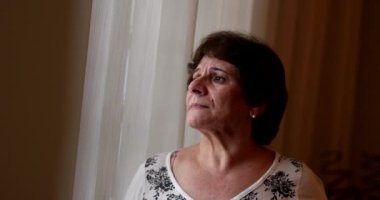 Contemplative senior woman looking through window, anxious depressed older lady