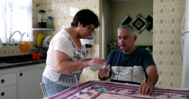 Middle aged couple at home, wife serving water to husband and giving pills to drink