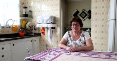 Düşünceli yaşlı kadın ev mutfağında oturuyor. Düşünceli, orta halli biri.