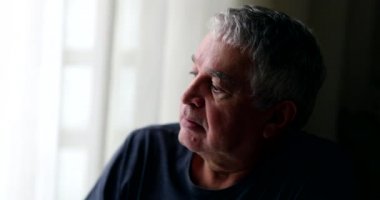 Bunalımda olan orta yaşlı bir adam evde oturup pencereden bakıyor.