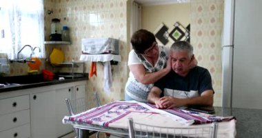Older wife standing by senior troubled husband at home