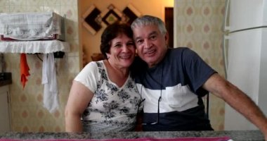 Happy older couple smiling at camera. Married senior couple sitting at kitchen posing