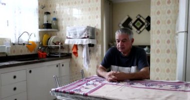 Thoughtful older man sitting at kitchen table. Pensive middle aged senior person