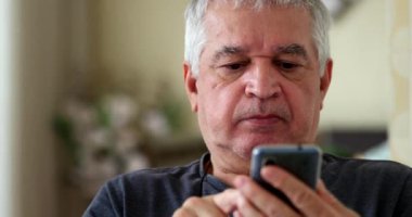 Evde cep telefonu kullanırken hayal kırıklığına uğramış bir ihtiyar. Akıllı telefona bakan yaşlı kişi üzgün.