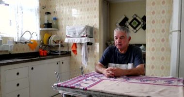 Yaşlı adam mutfak masasında tek başına oturuyor.