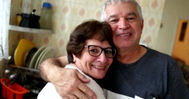 Ev mutfağında kameraya gülümseyen mutlu evli çift. Sıradan otantik yaşlılar portresi
