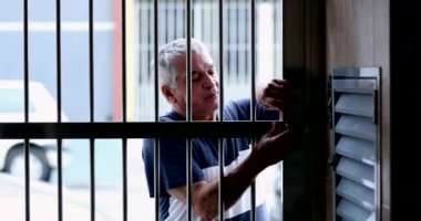 Older man opening metal gate entrance, person arriving home