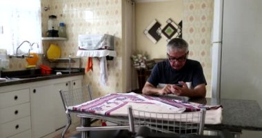 Senior man using cellphone at home kitchen. older person looking at smartphone