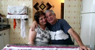 Happy older couple smiling at camera. Married senior couple sitting at kitchen posing